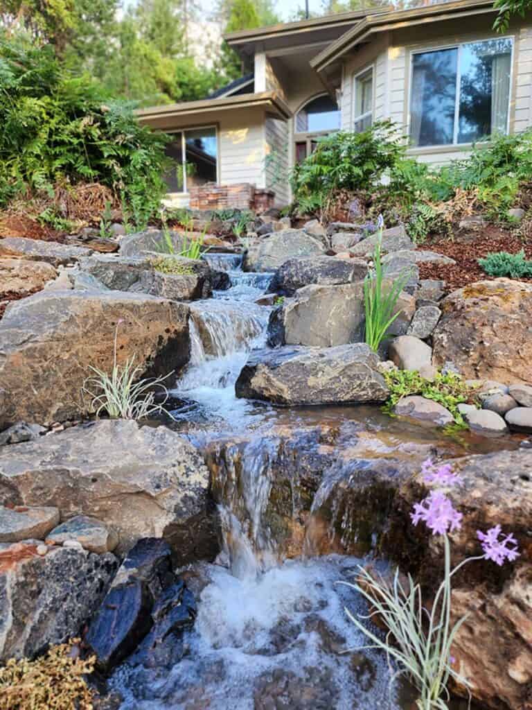 Cascading pondless waterfall with natural boulders beside a home